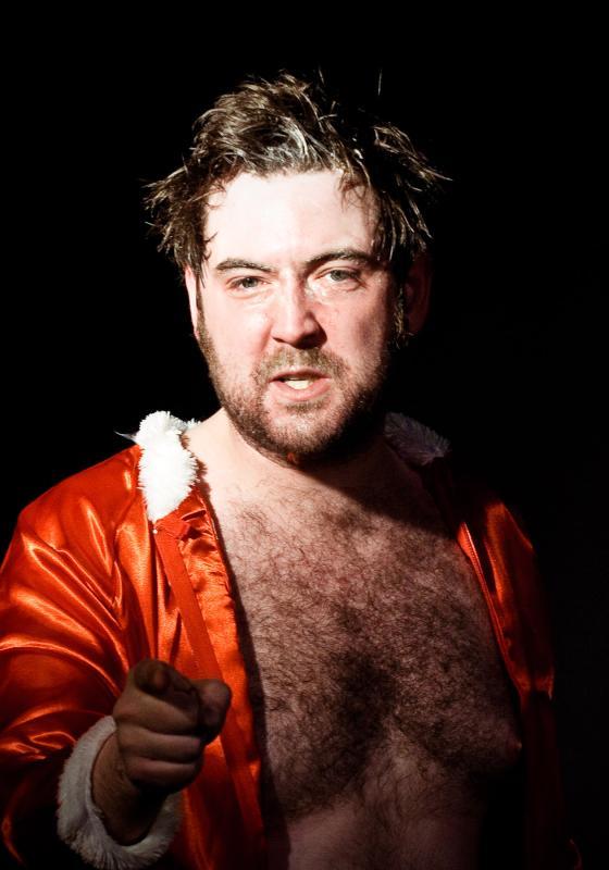 Nick, wearing a christmassy red shirt with white fur trim, points at the camera against a black background