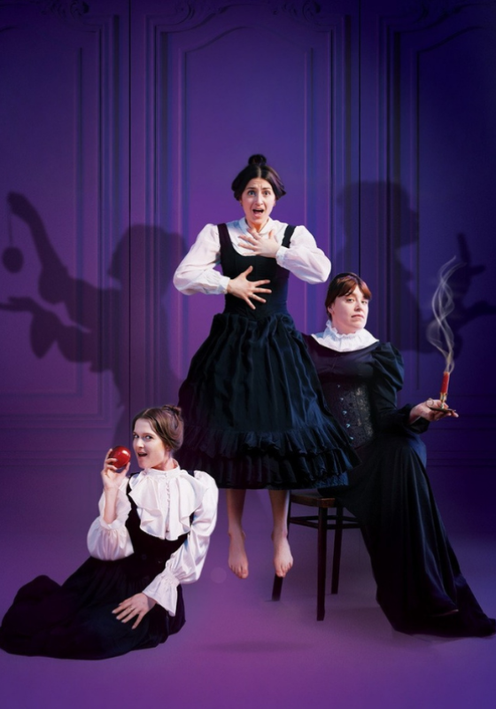 Three women in period dress: one holding an apple, one holding a lit dynamite and one levitating.