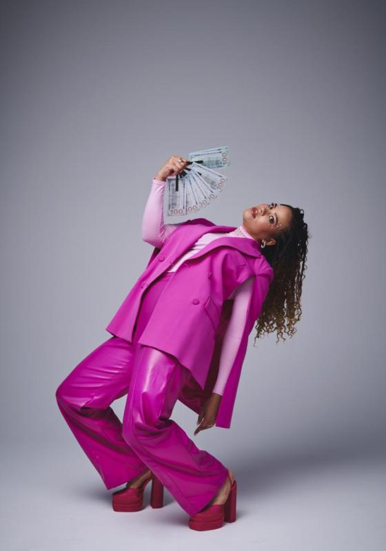 Mary bending backwards wearing a full pink suit and fanning herself with dollar bills