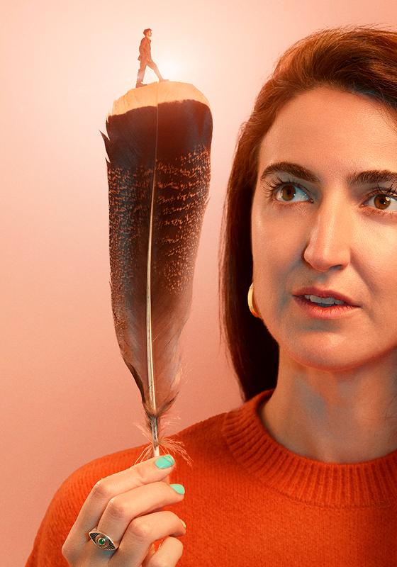 A woman holds a large bird's feather. A small figure walks over the top of the feather.  