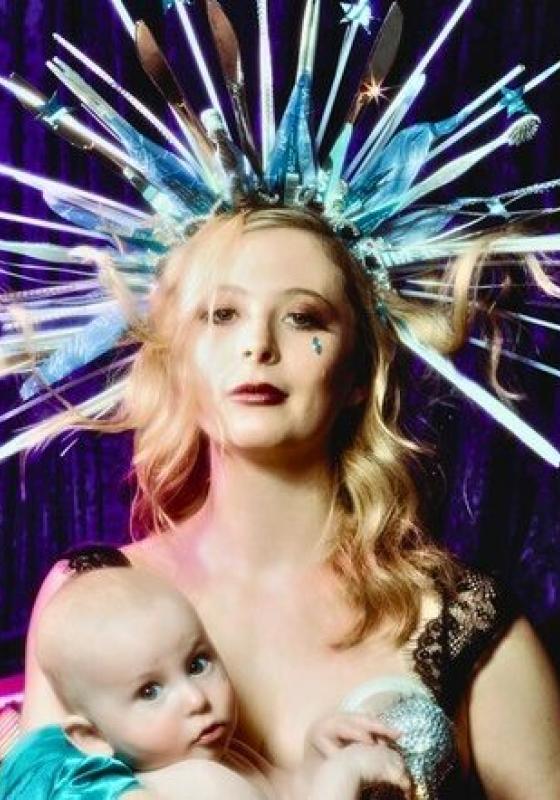 A woman holding a baby with wavy blonde hair is wearing a spiked crown