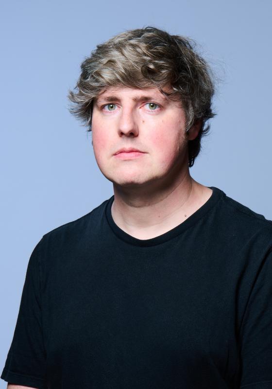 A picture of Glenn, wearing a black t shirt, against a light blue background.