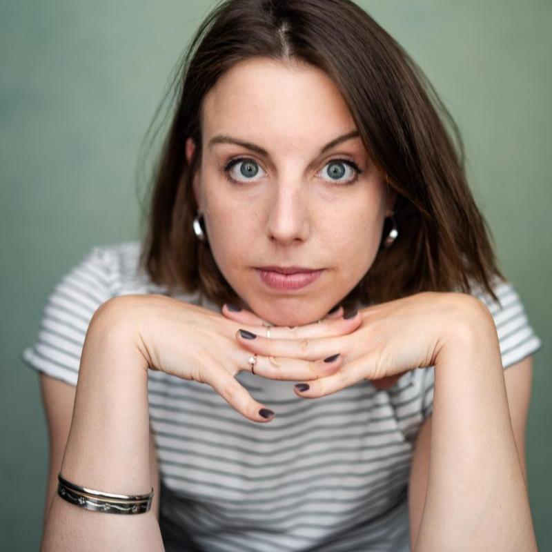 A headshot of Isobel as she looks directly into the camera. Her head is resting on her hands and she is wearing a striped t-shirt and silver jewelry. 