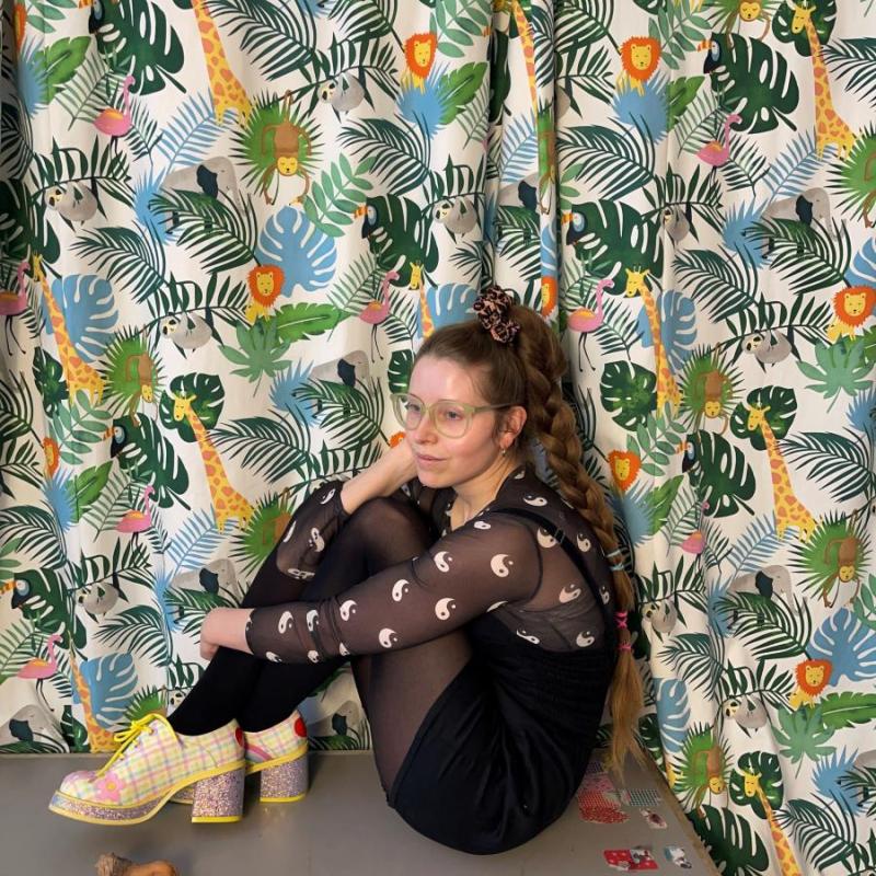 Jessie curled up in a corner against a colourful jungle backdrop and toy animals on the floor