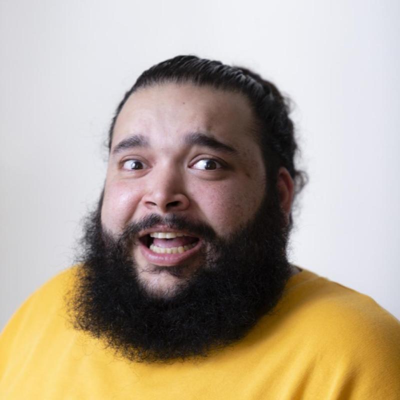 Headshot of a surprised and slightly anxious looking Raj with a lovely full beard and wearing a vivid yellow jumper.