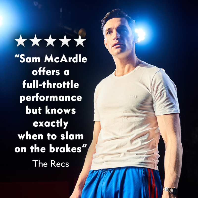The Manny stands on the stage in a white t-shirt and blue tracksuit bottoms speaking to the audience. The reviews text reads as  " 5 stars-Sam McArdle offers a full throttle performance but knows exactly when to slam on the brakes - The Recs"