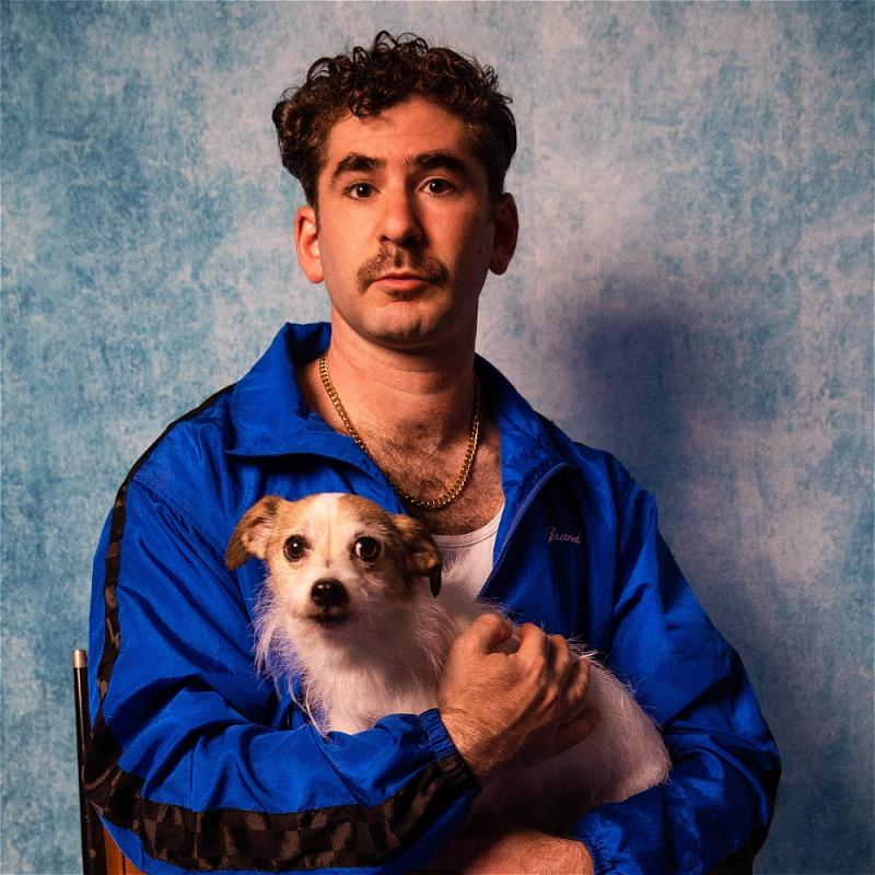 Josh Glanc in an 80s-esque school photo holding a dog and looking directly at the viewer.