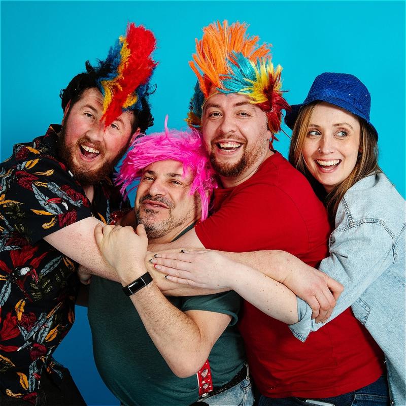 Four performers wearing colourful spiky wigs embrace with big smiles