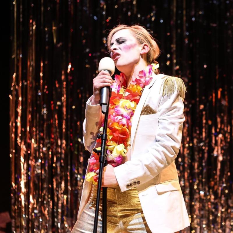 Marie Hamilton as Captain Macheath sings menacingly in a white fringed jacket and golden trousers 