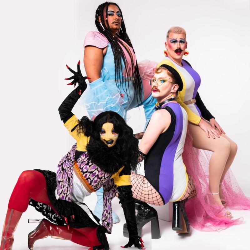 A studio shot of drag performers in costume; Bard the Beholder, Cyro, Flick and Carrot, all looking sassy and posing at different heights and levels. They are giving gender in different transient forms.