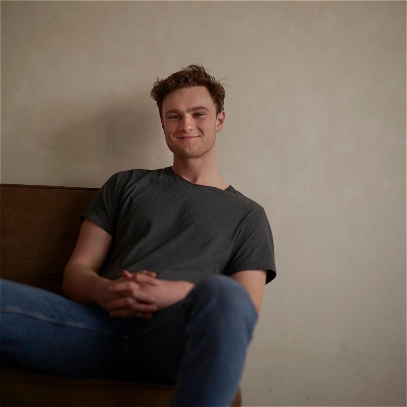 Josh lounging on a sofa with a gentle smile at the camera.