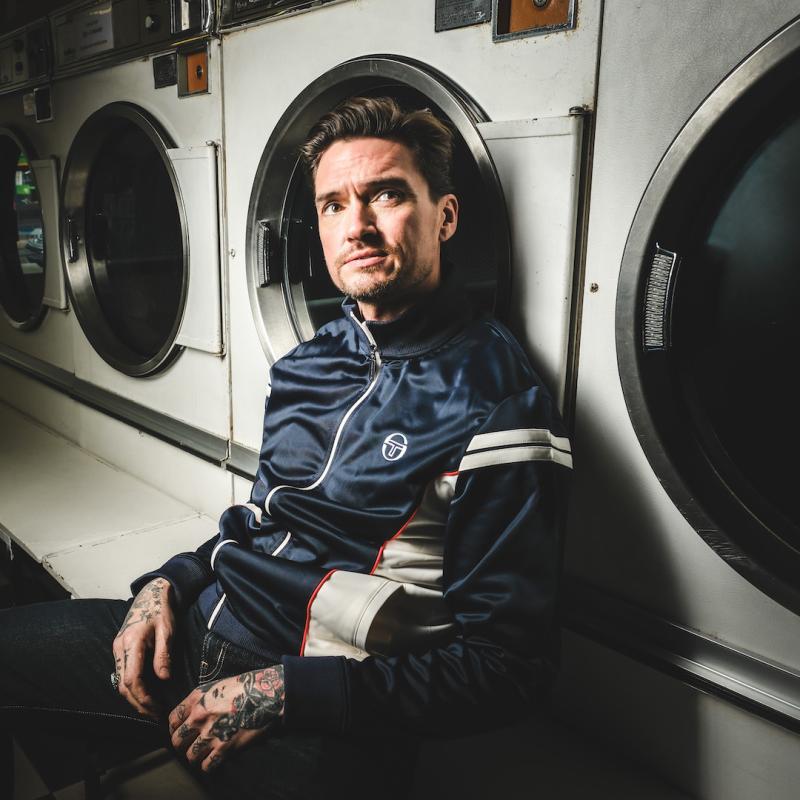 Jack sits in front of three launderette-style washing machines, looking upwards with a serious expression