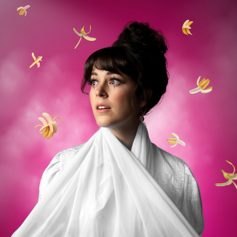 Woman with dark hair up in a bun, wearing a white scarf, gazing upward against a pink background with floating yellow banana shapes.