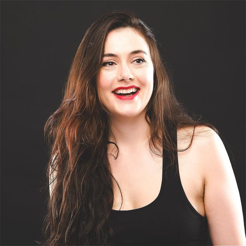 Marjolein laughingly looks over to the right, they have long brown hair and are wearing a black tank top.