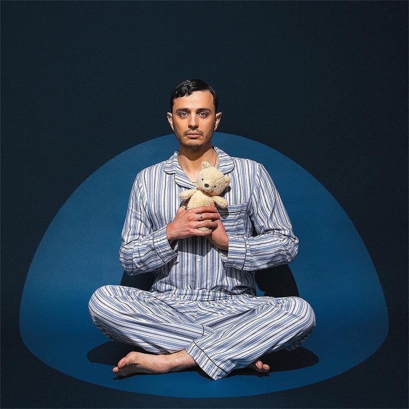 Pedro in blue and white striped pajamas sits cross-legged, holding a stuffed animal against a dark blue backdrop.