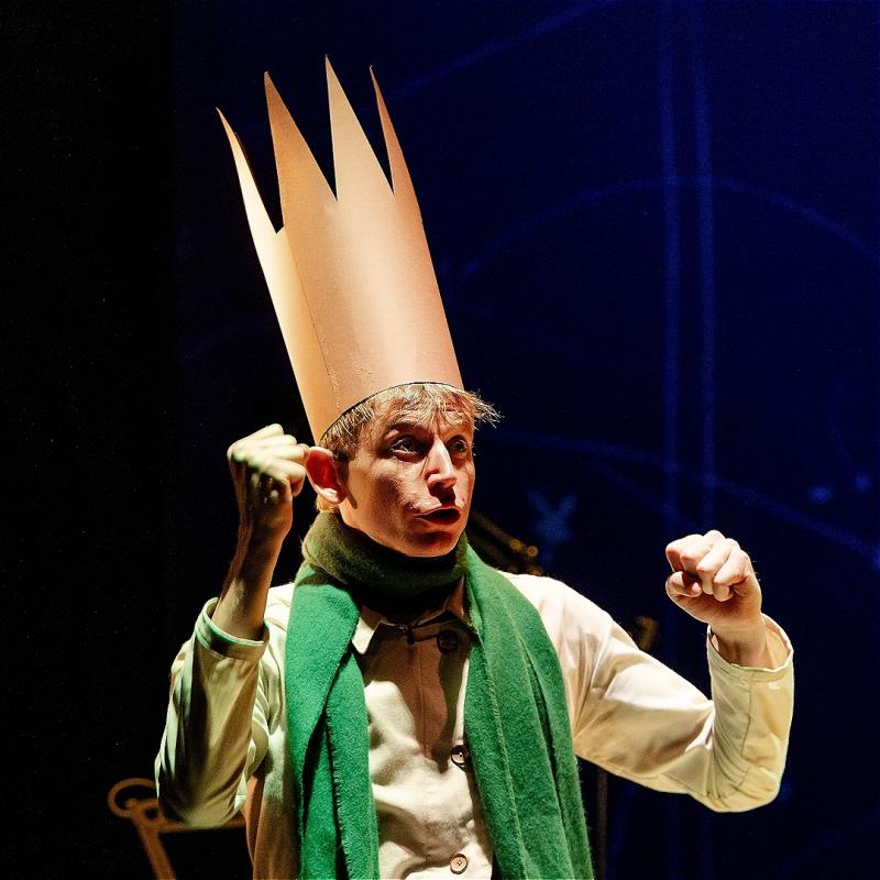 The performer wearing a tall crown and green scarf.