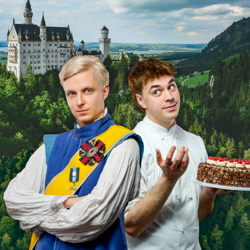 The prince looking into the camera whilst the baker looks bewildered holding a black forest gateau