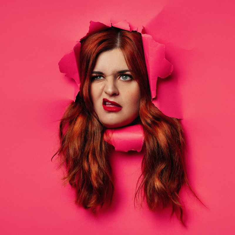Alex's disgruntled face, framed by auburn hair, bursts through a hot pink paper.