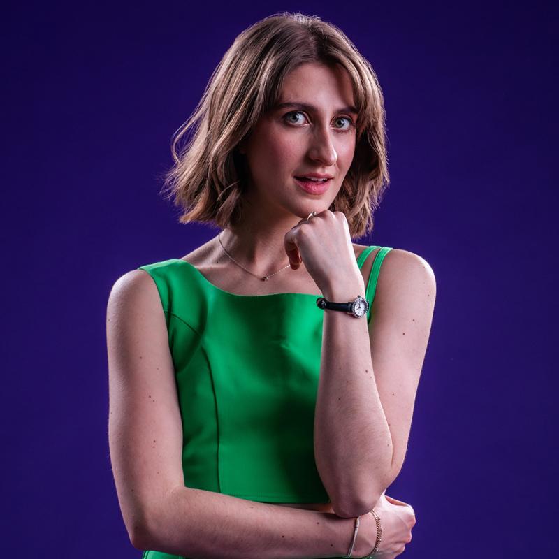 Anna wearing a green dress resting her chin on her hand subtly smiling at the camera.