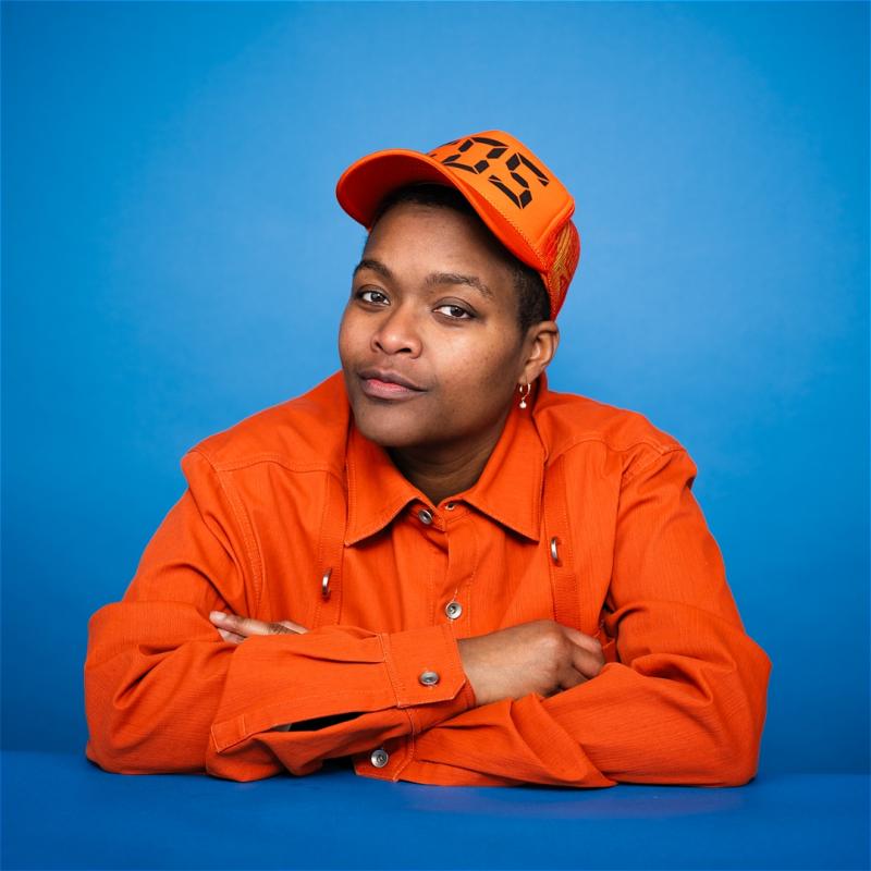 Sam jay in orange outfit against blue background