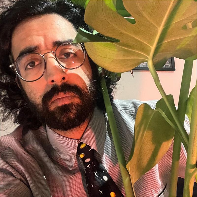 A bespectacled man sulks next to a plant