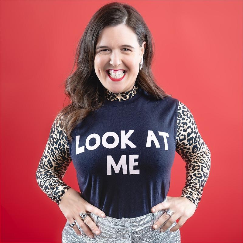 Rosie Jones stares at the camera with a brilliant smile and a top that says 'LOOK AT ME' in bold white letters