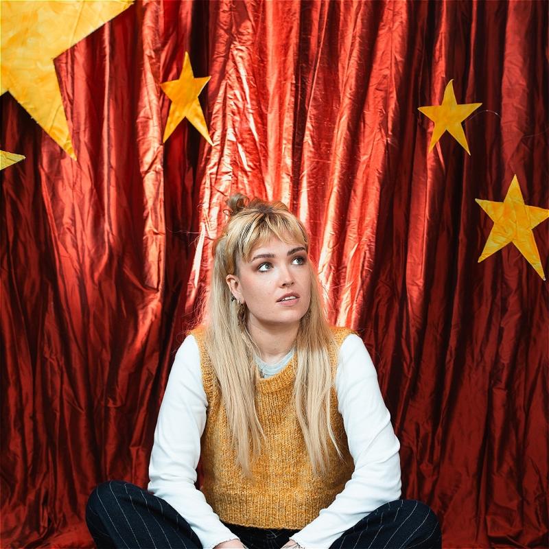 Performer sits in front of a red cloth background with stars cut out.