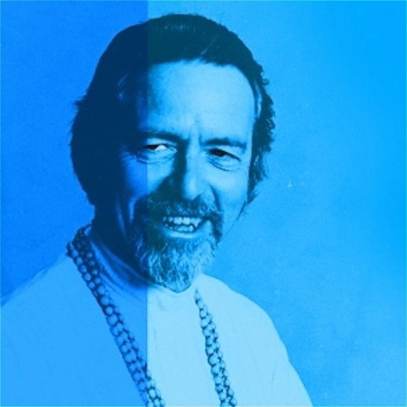 A man in a white shirt with a greying beard grins slyly off-camera. The photo has a blue filter.
