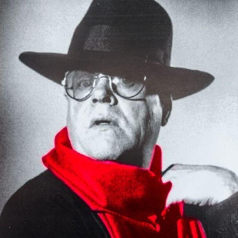 Black and white photo of Truman Capote wearing a hat and bright red scarf.