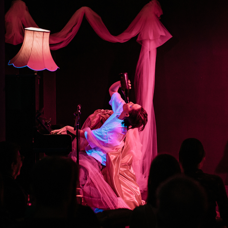 A performer drinks a bottle whilst playing a piano.