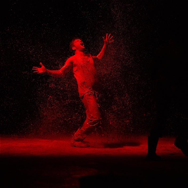 A performer covered in red dust cries out in anguish.