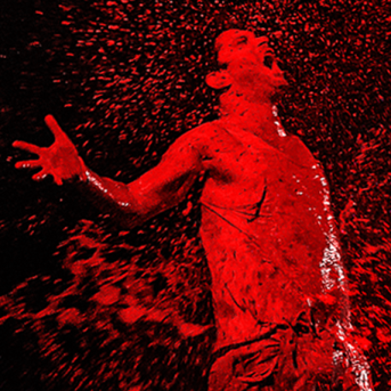 A performer covered in red paint cries out in anguish.
