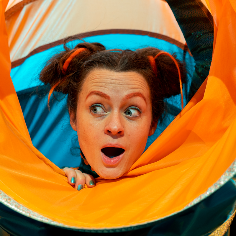 A woman smiles peering out of a large orange and blue nylon tube