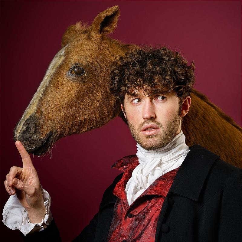 Christian looking perplexed whilst he holds a finger up by a horse