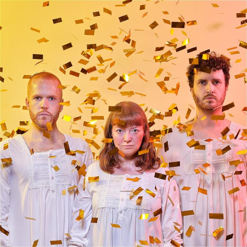 The cast of Tarot in long white dresses staring deadpan at the camera whilst it rains gold confetti