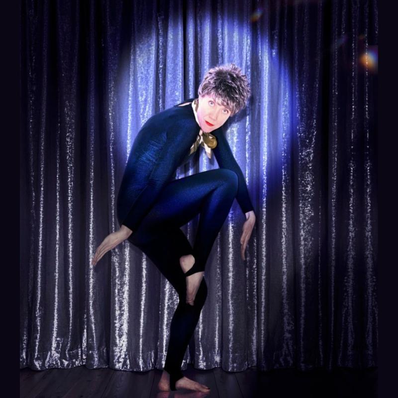 Dusty, wearing a black leotard, dances freely against a dark blue curtain with a spotlight on their face