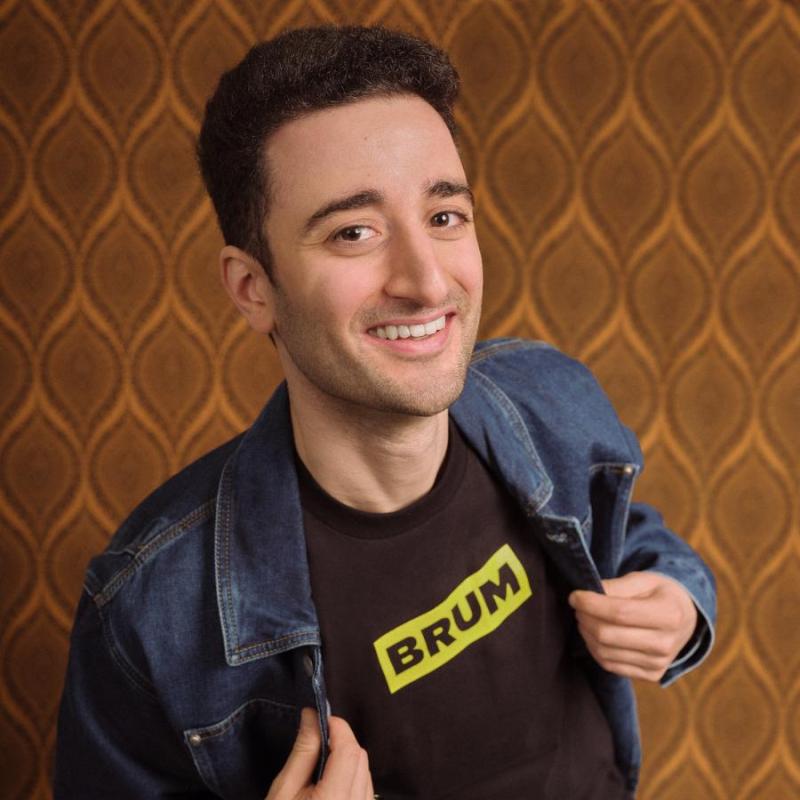 Hasan grinning whilst exposing his t-shirt with the word BRUM written on it.