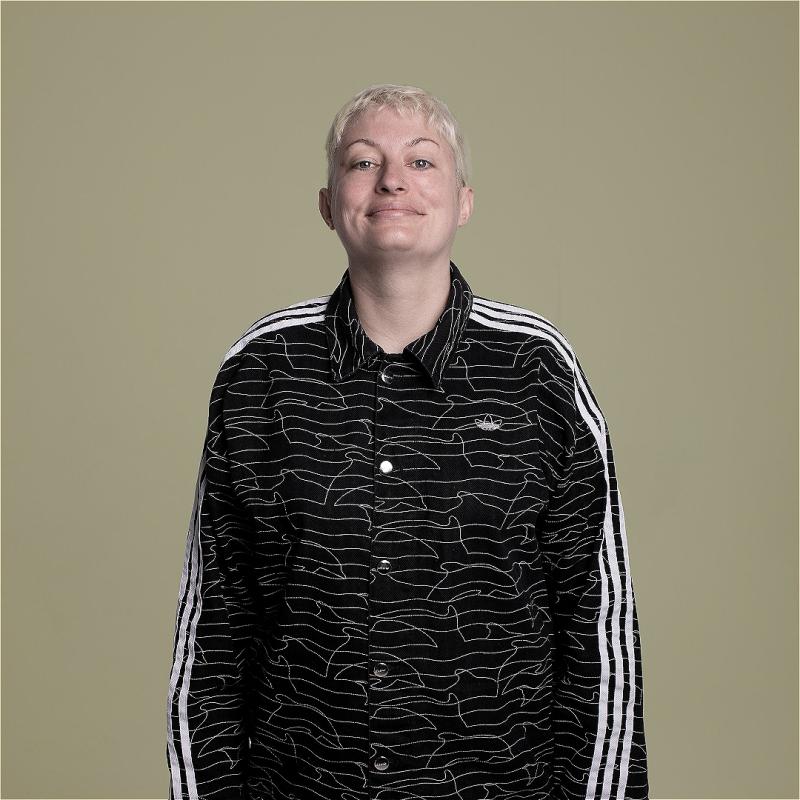 Harriet smiling at the camera with their arms by their sides against a grey backdrop