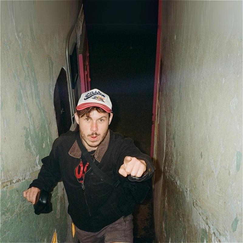 The image depicts someone walking through a narrow tunnel pointing to the camera.