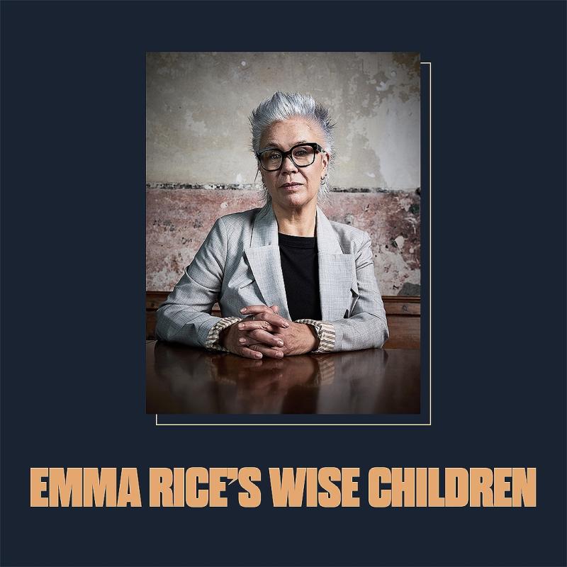 Emma Rice sat at a wooden table in front of a rustic looking wall, with text below reading "Emma Rice's Wise Children"