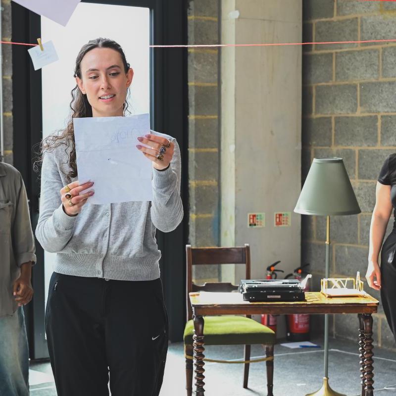 three women on stage, one is holding and reading a letter