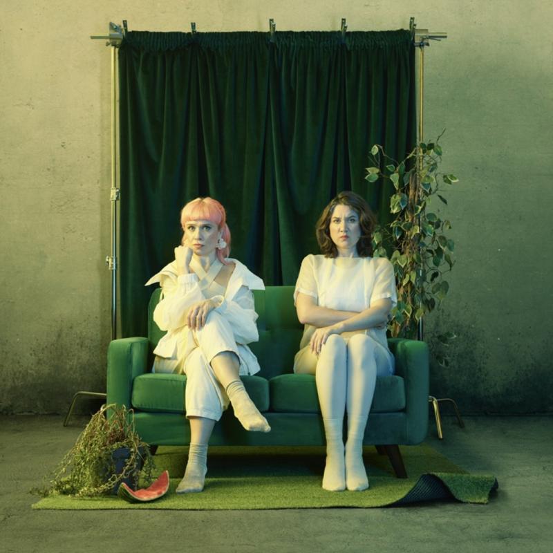The performers sitting awkwardly on a green sofa dressed in white. The photo has a green, haunting tint.