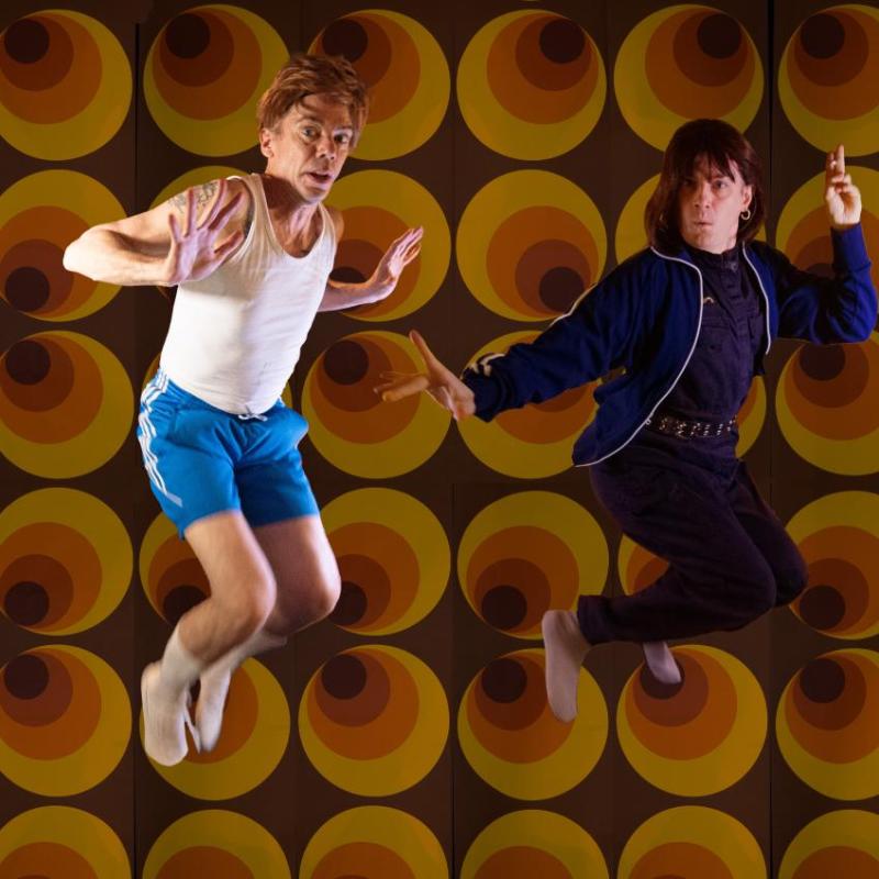 Two performers mid-air against a 70's style backdrop.