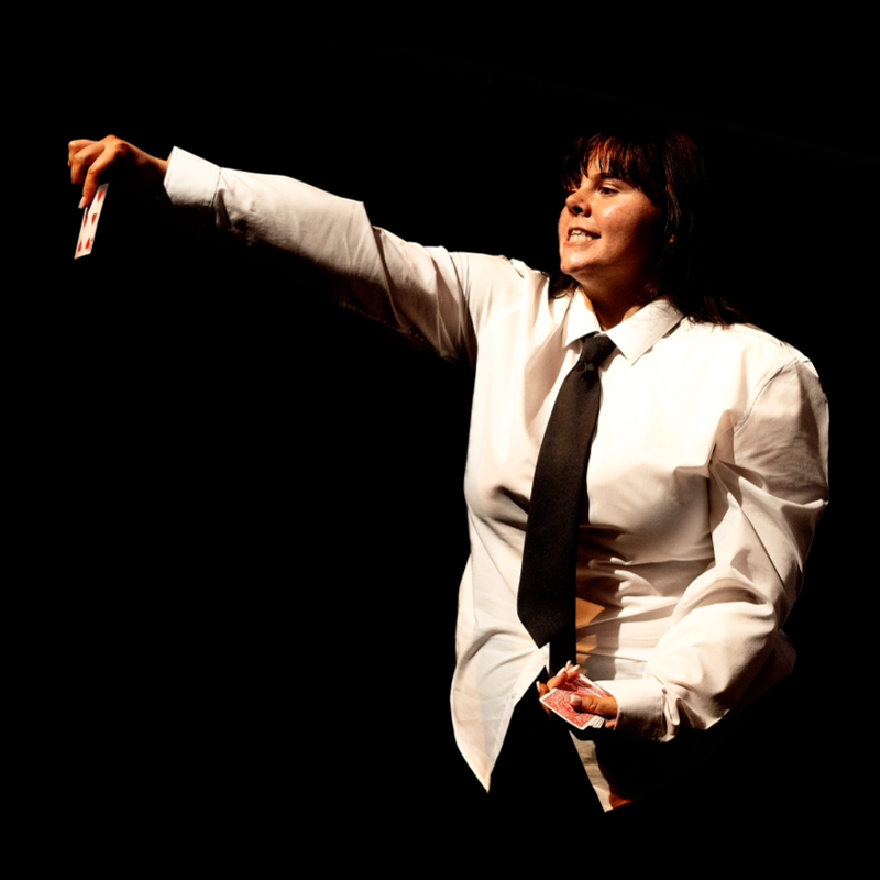 A performer in a suit holding up a card to the audience, the rest of the pack in their other hand.