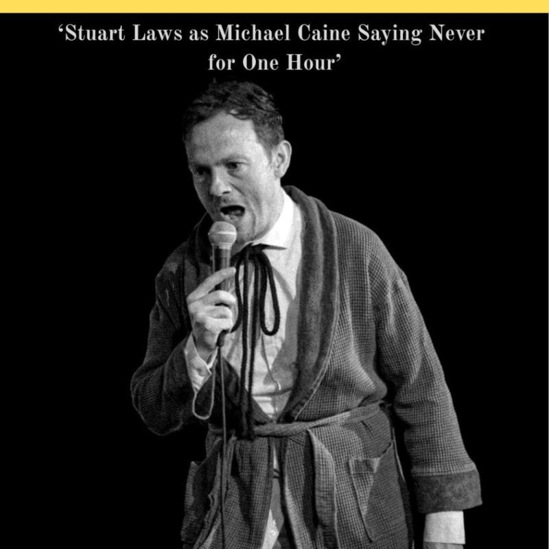 Stuart Laws in black and white wearing a dressing gown and holding a microphone.