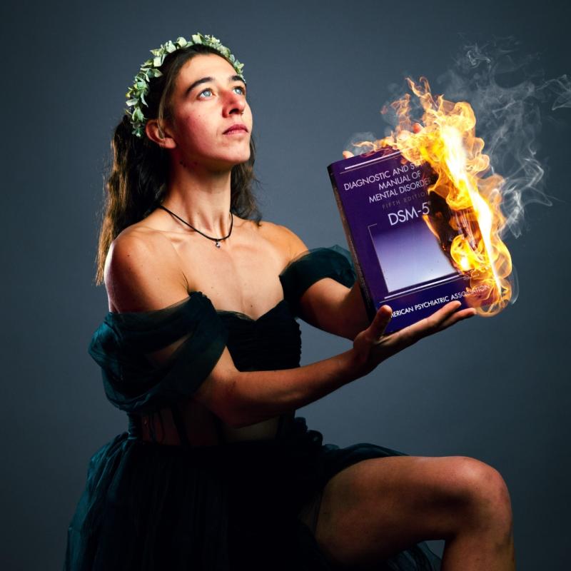 Performer kneels in a black dress and holds a burning book.