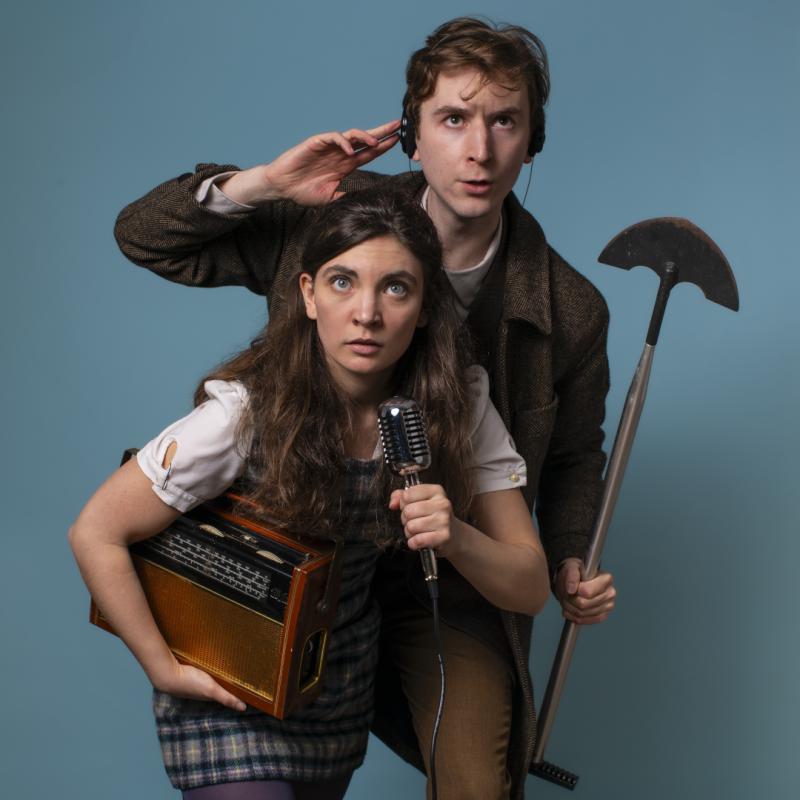 A man and a woman sleuths, one holds a microphone, the other a shovel. They look inquisitive.