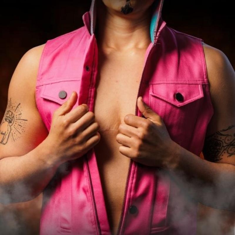 A performer wears a pink leather waistcoat over a bare chest as steam rises.