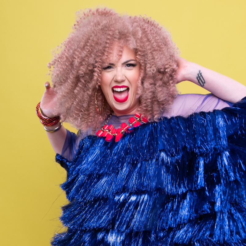 Frisky wearing a statement red necklace and a large dark blue flapper dress.
