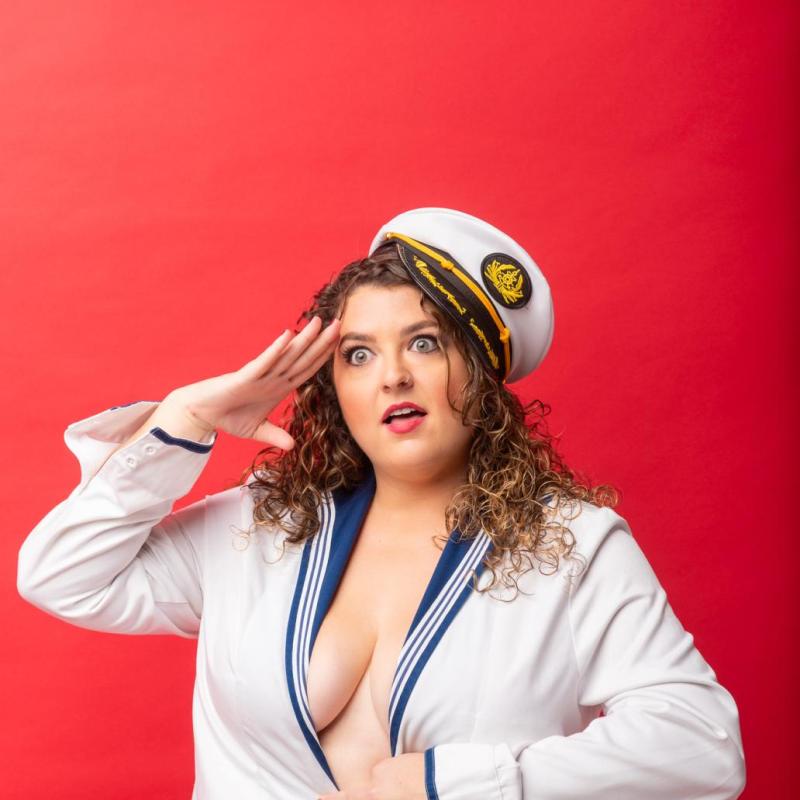 Mel McGlensey salutes whilst wearing a low-cut sailors uniform.